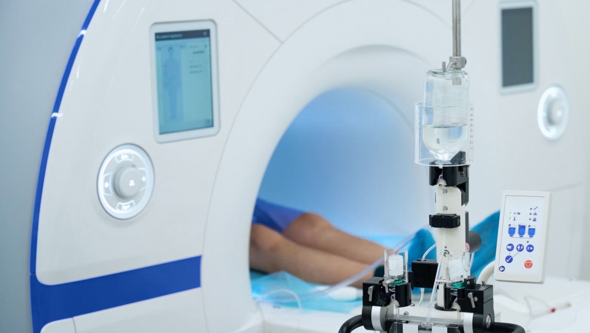 A patient's legs are visible entering a MRI machine, with medical equipment standing in the foreground